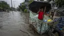 Seorang gadis memegang payung dan berjalan di atas gerobak melalui jalan yang banjir saat hujan deras di Guwahati, negara bagian Assam, India, Kamis (16/6/2022). (AP Photo/Anupam Nath)