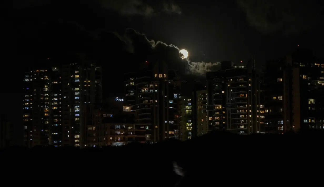 Seorang wanita berjalan dengan smartphone-nya saat sebagian bulan purnama tertutup awan di langit di Hadera, Israel, 14 Juni 2022. Fenomena ini disebut juga sebagai Strawberry Supermoon karena terjadi pada saat panen strawberry. (AP Photo/Ariel Schalit)