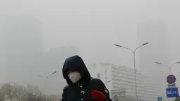 Seorang wanita beraktivitas mengenakan masker di sebuah jalan yang diselimuti kabut asap tebal di Beijing, China (14/11). Pihak berwenang mengeluarkan peringatan kuning untuk polusi udara buruk pada hari Rabu. (AP Photo/Andy Wong)