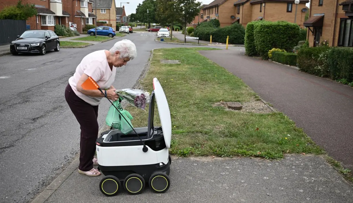 Sheila (71) mengambil kiriman dari robot otonom bernama Starship yang mengantarkan bahan makanan dari supermarket Co-op di Milton Keynes, Inggris, 20 September 2021. Robot Starship bertugas mengantarkan belanja dan makanan. (DANIEL LEAL-OLIVAS/AFP)