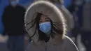 Seorang wanita mengenakan masker untuk membantu mengekang penyebaran virus corona bersiap menghadapi angin dingin saat dia berjalan di dekat distrik perbelanjaan Wangfujing di Beijing, Minggu (12/12/2021). (AP Photo/Andy Wong)