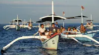 Wisatawan di atas perahu selama tamasya menyaksikan lumba-lumba di perairan Pantai Lovina di Singaraja, Bali, Jumat (30/10/2020). Pantai Lovina merupakan salah satu destinasi pariwisata di Bali yang sering dikunjungi untuk menikmati matahari terbit dan lumba-lumba di laut lepas (SONNY TUMBELAKA/AFP)