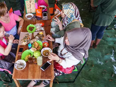 Pengunjung menikmati makan siang sambil digigit ikan dikakinya di restoran kolam ikan di desa Wedomartani di Yogyakarta (15/11/2019). Restoran unik ini dikenal dengan nama Soto Cokro Kembang. (AFP Photo/Oka Hamied)