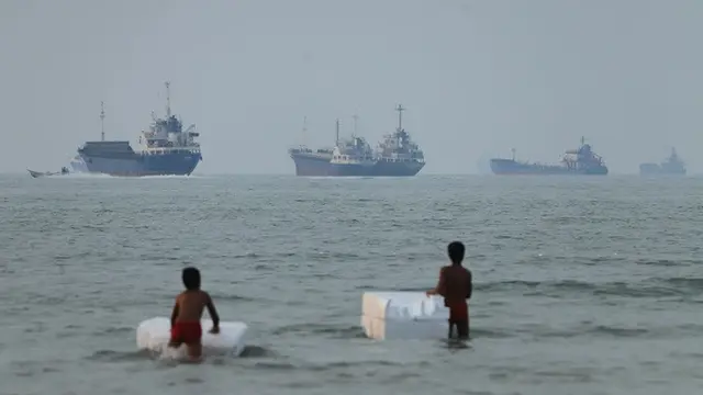 Dua anak laki-laki bermain di perairan dangkal di lepas pantai Bandar Abbas, Iran, dengan latar kapal-kapal yang melintas di Selat Hormuz, Selasa (30/6/2026).