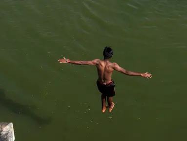 Seorang pemuda India melompat ke dalam sungai yang tercemar di pinggiran Chennai, India, Rabu (5/4). Sejumlah warga di India biasa mandi di sungai saat cuaca panas. (AFP PHOTO / ARUN SANKAR)