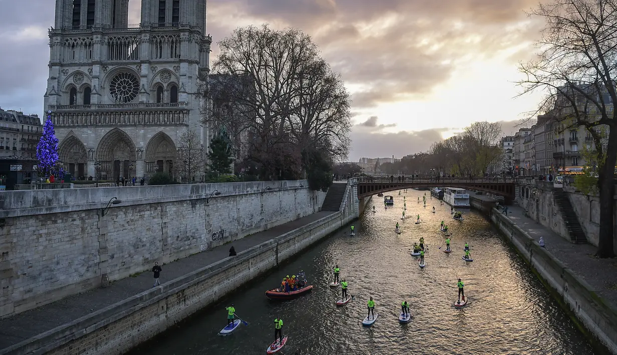 Para peserta mengambil bagian dalam Nautic Paddle Race dekat katedral Notre-Dame di Paris, Minggu (9/12). Sekitar 800 orang mengikuti lomba dayung sambil berdiri terbesar di dunia sejauh 11 km menyeberangi sungai Seine. (Lucas BARIOULET/AFP)