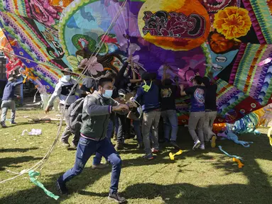 Warga membantu mengangkat layang-layang raksasa untuk ditampilkan pada Hari Semua Orang Kudus sebagai bagian dari perayaan Hari Kematian di Santiago Sacatepequez, Guatemala, 1 November 2021. Perayaan digelar dengan sejumlah pembatasan untuk mengekang penyebaran COVID-19. (AP Photo/Moises Castillo)