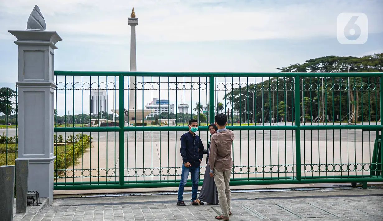 Warga berfoto di belakang Monumen Nasional atau Monas di Jakarta, Jumat (1/1/2021). Walaupun Monas ditutup warga tetap memanfaatkan libur Tahun Baru untuk berwisata dan berfoto di kawasan Monas. (Liputan6.com/Faizal Fanani)