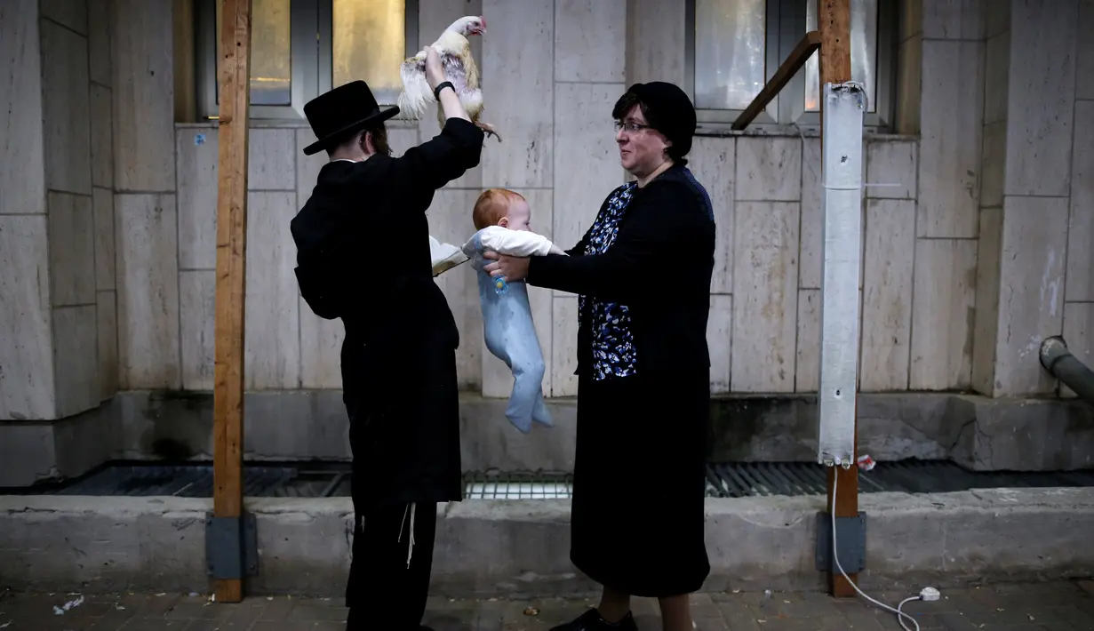 Seorang pria Yahudi Ultra-Ortodoks memegang ayam di atas kepala bayi saat melakukan ritual Kaparot, di Ashdod, Israel, (9/10). Dalam ritual ini ayam putih disembelih sebagai syarat simbolis dari penebusan. (REUTERS/Amir Cohen)