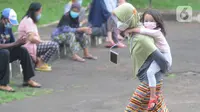 Pasien Covid-19 menggendong seorang anak melintas di halaman Graha Wisata Ragunan, Jakarta, Selasa (15/6/2021). Pemprov DKI memfungsikan kembali Graha Wisata Ragunan sebagai tempat isolasi warga terpapar COVID-19 kategori OTG sejak pekan lalu dan saat ini merawat 117 pasien (merdeka.com/Arie Basuki)