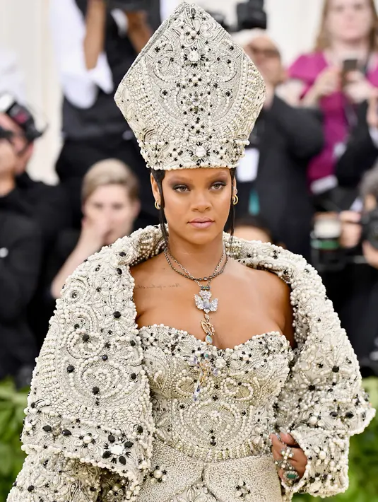 Penyanyi Rihanna berpose untuk fofotgrafer setibanya pada pagelaran Met Gala 2018 di Museum Seni Metropolitan New York, Senin (7/5). Menyempurnakan gayanya, aksesori di kepalanya yang menyerupai mitre atau mitra. (Charles Sykes/Invision/AP)