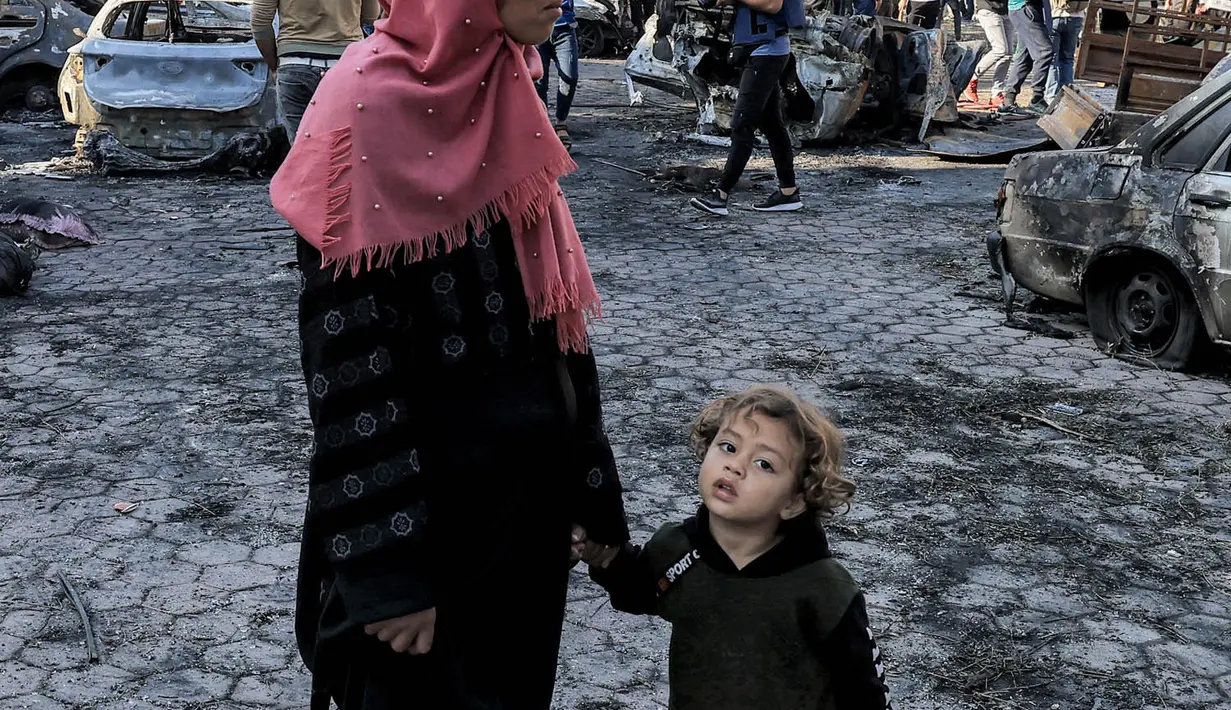 <p>Seorang wanita berdiri bersama seorang anak perempuan di luar lokasi rumah sakit Ahli Arab di pusat kota Gaza pada 18 Oktober 2023. (MAHMUD HAMS/AFP)</p>