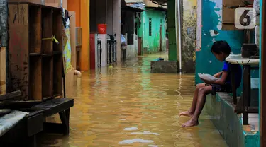 Seorang anak menikmati makanan saat banjir di kawasan Bidara Cina, Kecamatan Jatinegara, Jakarta Timur, Selasa (25/2/2020). Baru satu hari air surut, kawasan Bidara Cina yang bersebelahan dengan Kali Ciliwung kembali mengalami banjir. (merdeka.com/magang/ Muhammad Fayyadh)