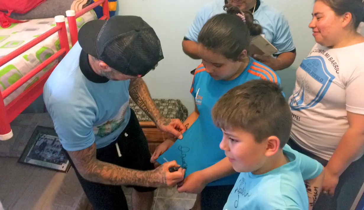 David Beckham memberikan tanda tangan untuk anak-anak di kawasan pemukiman kumuh 1-11-14 di Buenos Aires, Senin (9/11/2015). Beckham berada Argentina untuk membuat film dokumenter tentang sepak bola. (AFP/FIXER-Argentina/Macarena GAGLIARD)