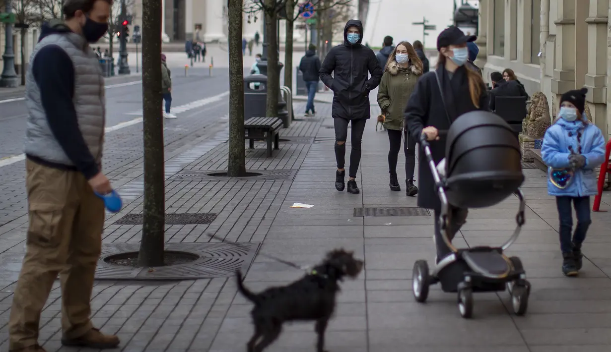 Penduduk lokal yang mengenakan masker wajah untuk melindungi dari virus korona, berjalan di Gediminas Avenue di Vilnius, Lithuania (7/11/2020). Penguncian dilakukan untuk membendung penyebaran virus corona. (AP Photo/Mindaugas Kulbis)
