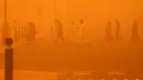 <p>Pejalan kaki menyeberang jalan di tengah badai debu parah di Kuwait City pada 23 Mei 2022. Gumpalan debu besar yang melayang di atas Kuwait telah mengurangi visibilitas menjadi hampir nol di jalan-jalan hampir sepanjang hari di seluruh negeri. (Yasser Al-Zayyat / AFP)</p>