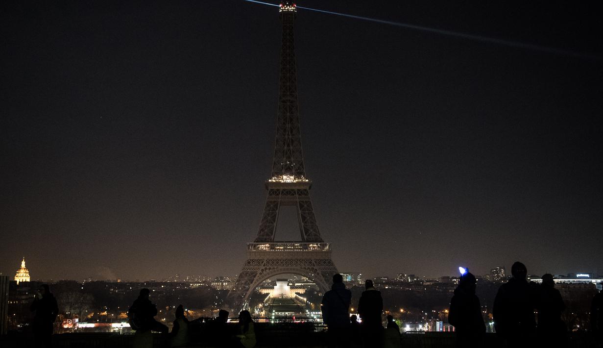 Sejumlah wisatawan mengamati pemadaman lampu di Menara Eiffel, Paris, Rabu (14/12). Lampu menara ikonik setinggi 300 meter itu dimatikan pada Rabu malam untuk menunjukkan dukungan bagi warga Aleppo di Suriah. (AFP PHOTO/PHILIPPE LOPEZ)