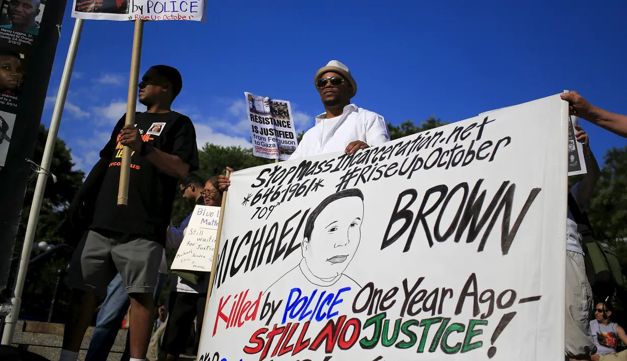 Warga membawa poster saat aksi memperingati satu tahun pembunuhan remaja kulit hitam yang tidak bersenjata, Michael Brown oleh polisi berkulit putih yang memicu kerusuhan besar, di Ferguson, New York, Minggu (9/8/2015). (REUTERS/Eduardo Munoz)