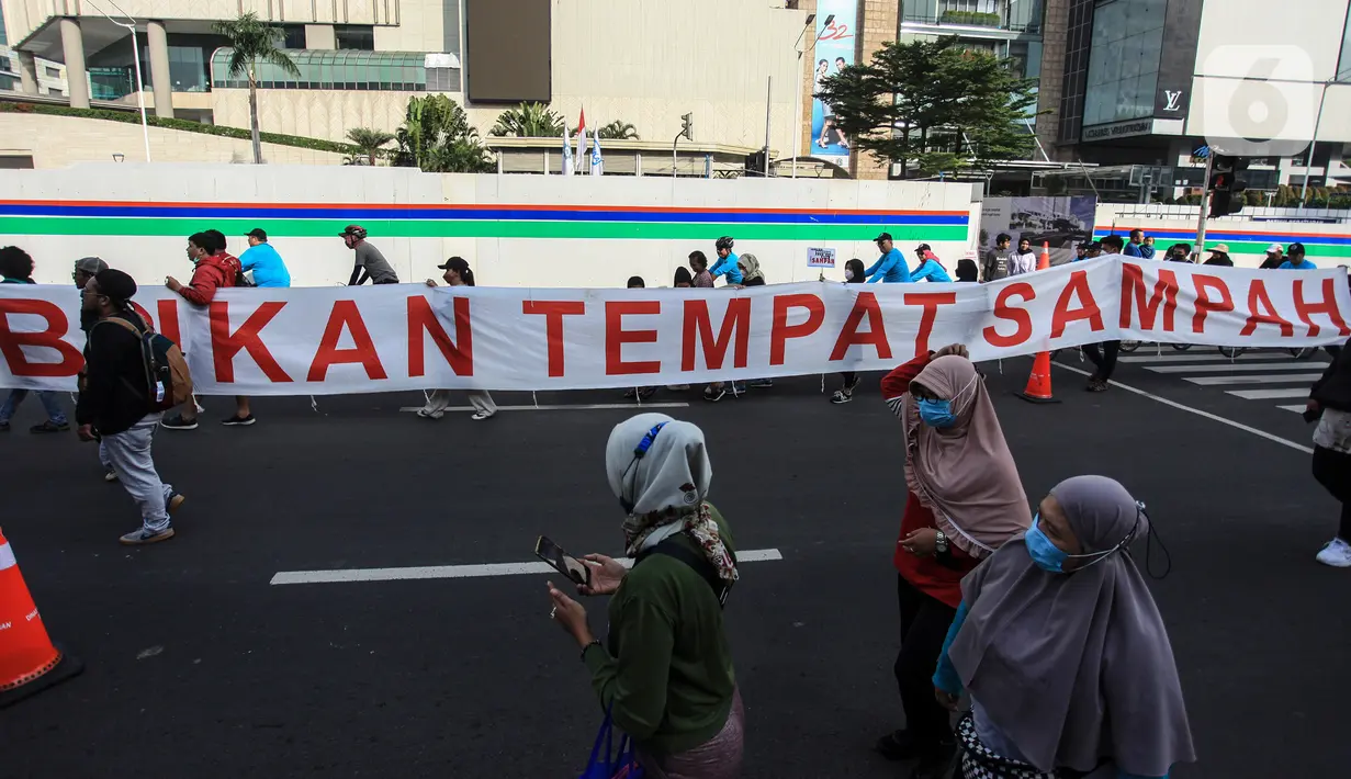 Pengunjung melintas saat warga dari Komunitas Peduli Sampah menggelar aksi saat Hari Bebas Kendaraan Bermotor di Bundaran HI, Jakarta, Minggu (26/6/2022). Kampanye tentang sampah tersebut dalam rangka melanjutkan Pekan Gerakan Jakarta Sadar Sampah yang menghimbau masyarakat untuk saling menjaga kebersihan lingkungan. (Liputan6.com/Johan Tallo)
