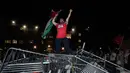 Seorang mahasiswa Universitas George Washington melambaikan bendera Palestina saat berdiri di atas barikade polisi yang diterobos untuk menduduki University Yard dalam aksi protes pro-Palestina di Washington, Minggu, 28 April 2024. (AP Photo/Cliff Owen)