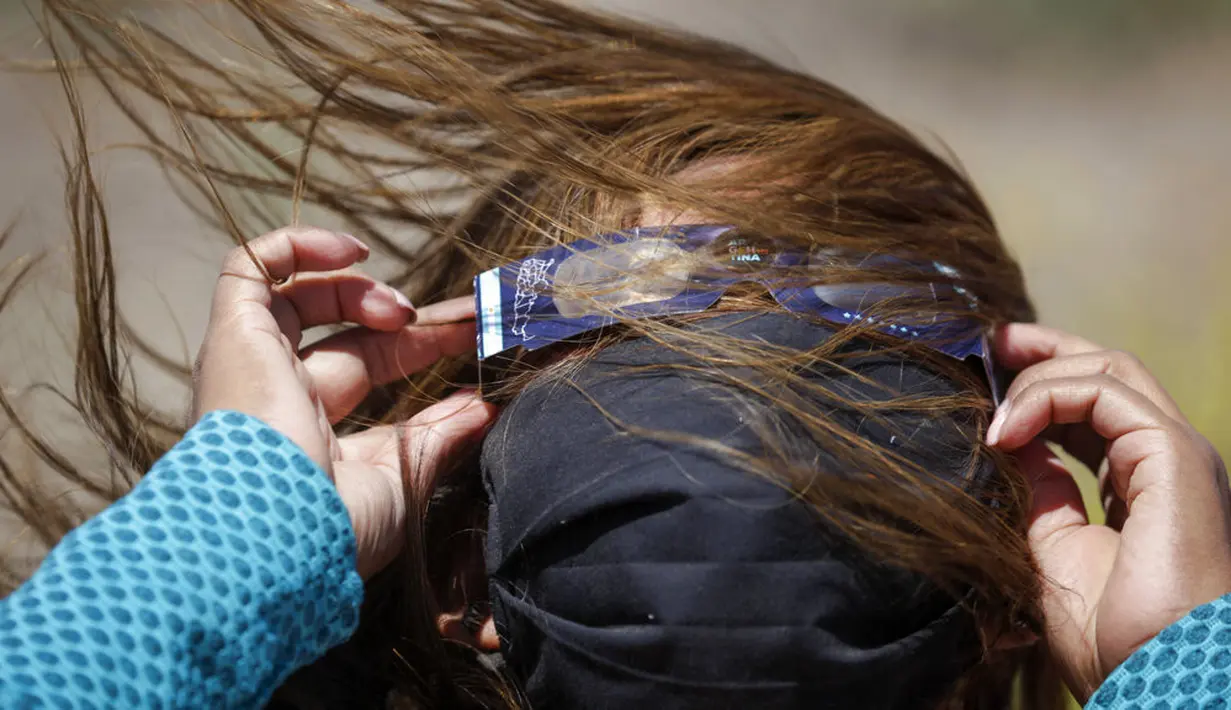 Seorang wanita mengenakan kacamata khusus untuk menyaksikan gerhana matahari total di Piedra del Aguila, Argentina, Senin (14/12/2020). Gerhana matahari total terlihat dari wilayah Patagonia utara Argentina dan dari Araucania di Chili. (AP Photo/Natacha Pisarenko)