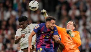 Kiper Barcelona, Wojciech Szczesny, meninju bola melewati Aurelien Tchouameni dari Real Madrid dan Eric Garcia dari Barcelona dalam pertandingan La Liga di Santiago Bernabeu, Minggu, 26 Oktober 2025. (AP Photo/Bernat Armangue)