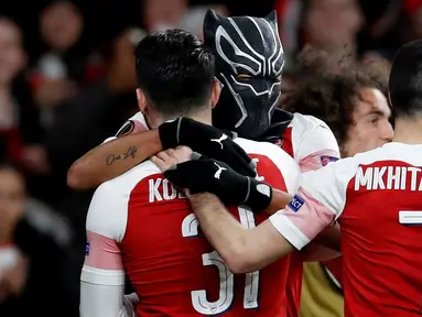 Striker Arsenal Pierre-Emerick Aubameyang mengenakan topeng superhero Black Panther memeluk rekannya usai mencetak gol ke gawang Stade Rennes pada leg kedua babak 16 besar Liga Europa di Stadion Emirates, London, Inggris  (14/3). (REUTERS/David Klein)