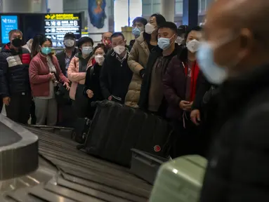 Pelancong yang memakai masker menunggu barang bawaan mereka di area kedatangan internasional di Bandara Internasional Ibukota Beijing di Beijing, Senin (9/1/2023). Pelancong internasional pertama tiba di China tanpa karantina wajib yang telah diberlakukan pada awal penerbangan. Pandemi tiga tahun lalu setelah pembatasan dicabut mulai hari Minggu. (AP/Mark Schiefelbein)