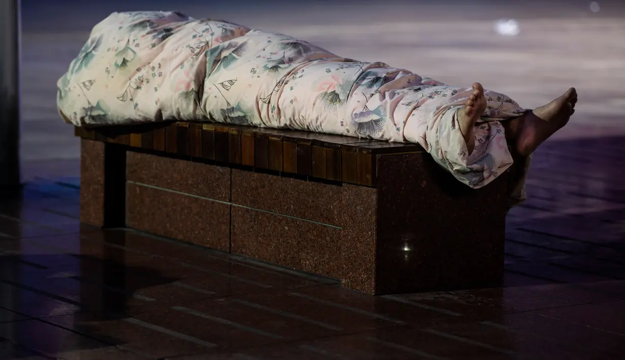 Seorang pria tidur di bangku di sepanjang Nanjing East Road, Shanghai (8/8). Selama musim panas, banyak rumah di beberapa daerah pemukiman rendah di Shanghai kekurangan pendingin udara. (AFP Photo/Johannes Eisele)