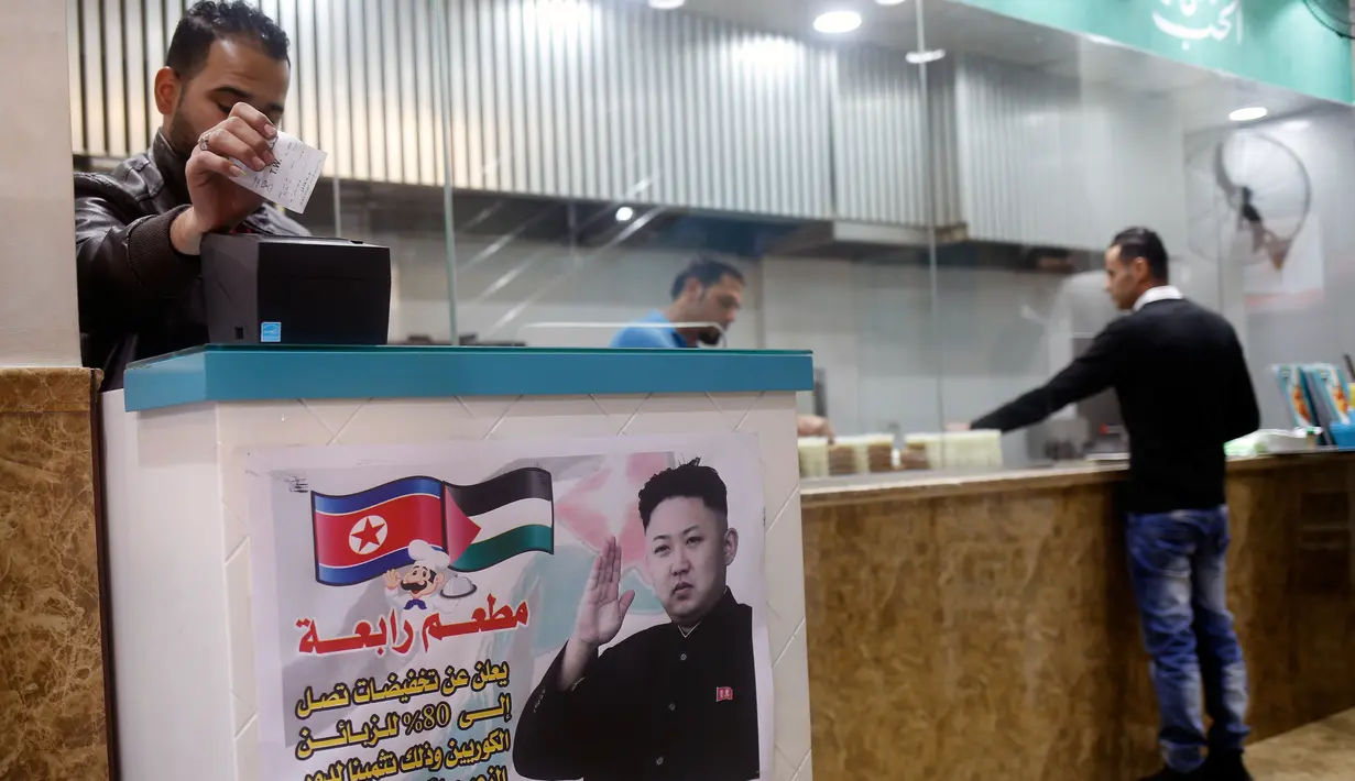 Seorang kasir menunggu di pintu masuk restoran Rabaa di kamp pengungsi Jabalia, Gaza, Minggu (17/12). Di restoran Rabaa terdapat poster pemimpin Korea Utara Kim Jong-Un dengan bendera Korea Utara dan bendera Palestina di sebelahnya. (MOHAMMED ABED/AFP)
