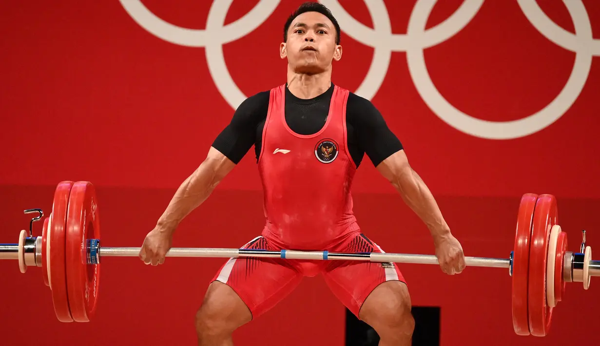 Lifter andalan Indonesia, Eko Yuli Irawan berusaha mengangkat beban saat bertanding dalam kelas 61kg putra Grup A cabor angkat besi Olimpiade Tokyo 2020 di Tokyo International Forum, Minggu (25/7/2021). Eko Yuli meraih medali perak dengan total angkatan 302 kg. (Vincenzo PINTO / AFP)