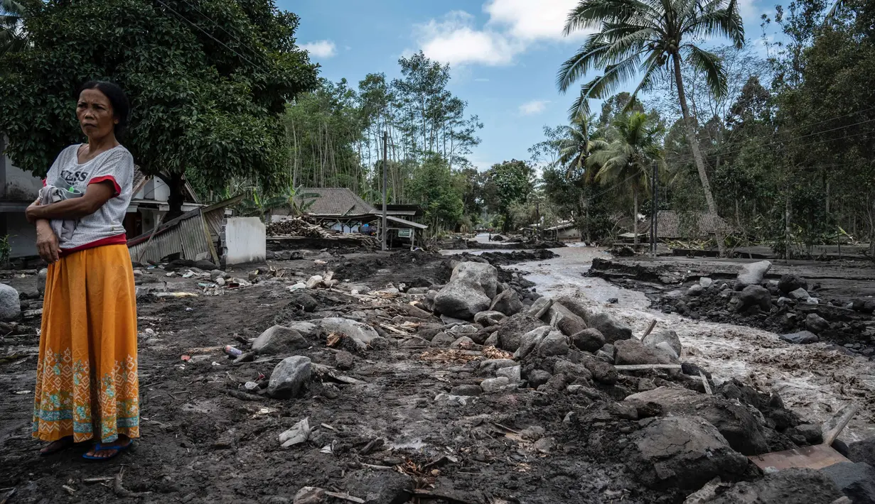 Seorang wanita berdiri dekat rumah yang rusak di Dusun Kamar Kajang, Lumajang, Kamis (9/12/2021). Puluhan rumah di dusun tersebut terendam luapan air sungai bercampur material lahar dingin erupsi Gunung Semeru akibat diguyur hujan deras pada Selasa (7/12) dan Rabu (8/12) malam. (Juni Kriswanto/AFP)
