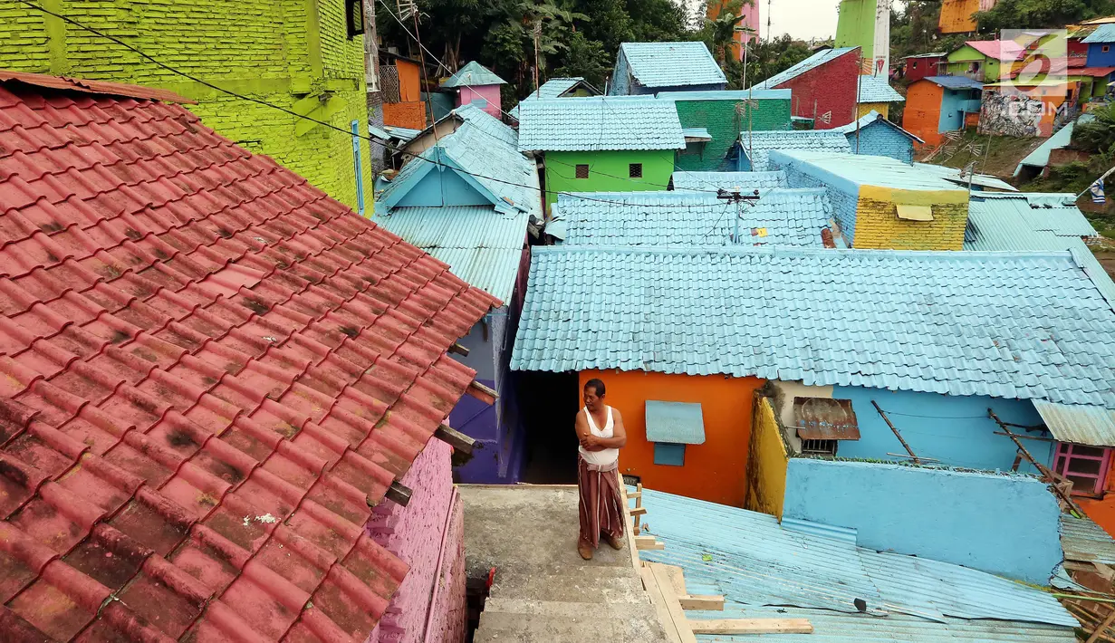 Seorang warga berdiri di tangga rumahnya di Kampung Warna-warni Jodipan dan Kampung Tridi (3D) di pinggir Sungai Brantas, Tumenggungan Ledok, Blimbing, Kota Malang, Jawa Timur (29/7). Kampung ini juga dipenuhi aneka mural. (Liputan6.com/Johan Tallo)