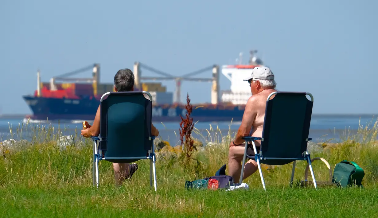 Warga berjemur ketika kapal kargo menuju Laut Utara saat suhu mencapai 34 derajat Celcius di dekat pantai Laut Utara di Wremen, Jerman barat (24/7/2019). (AFP Photo/Patrik Stollarz)