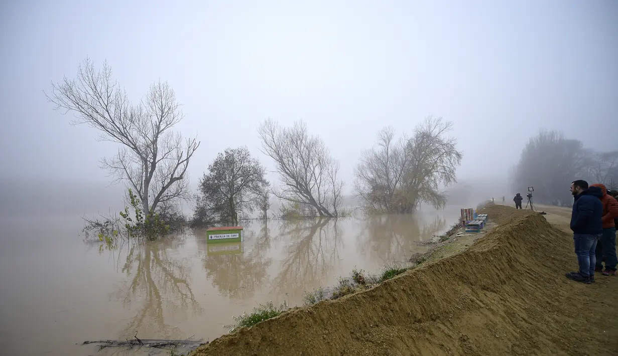 Orang-orang berdiri di samping perbatasan daerah banjir di dekat Sungai Ebro di desa kecil Pradilla de Ebro, provinsi Aragon, Spanyol utara (13/12/2021). Hujan deras menyebabkan banjir di Spanyol utara. (AP Photo/Alvaro Barrientos)