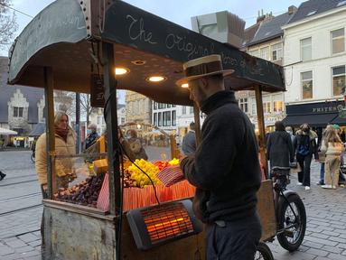 Seorang pedagang kaki lima menjual permen di shopping street di Ghent, Belgia, Rabu (22/12/2021). Belgia memutuskan untuk lebih memperketat pembatasan guna mengantisipasi varian Omicron yang melonjak tetapi menghindari lockdown penuh seperti yang dilakukan Belanda. (AP Photo/Virginia Mayo)