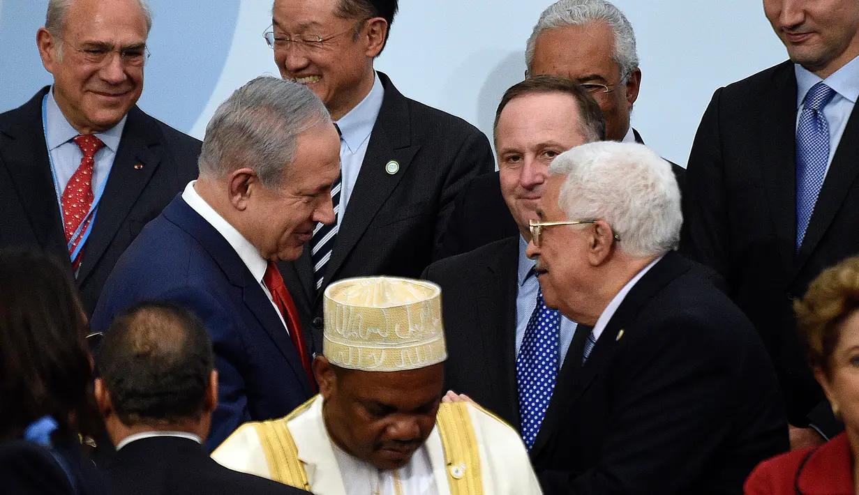 PM Israel Benjamin Netanyahu (kiri) berjabat tangan dengan Presiden Palestina Mahmud Abbas di depan Presiden Selandia Baru disela foto bersama pada KTT Perubahan Iklim, Conference of Parties (COP) 21 di Prancis, Senin (30/11). (AFP/POOL/MARTIN BUREAU)