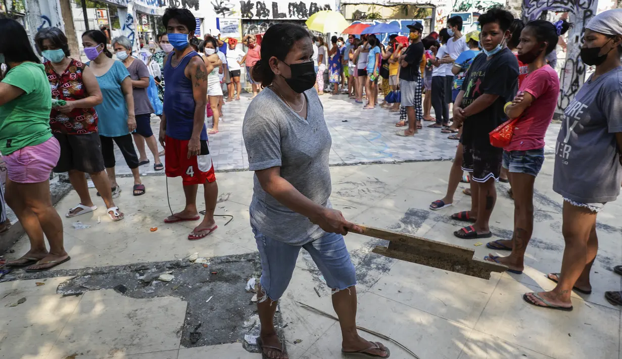 Seorang wanita memegang sebatang kayu saat dia meminta penduduk lain untuk menjaga jarak sosial saat mereka mengantre untuk mendapatkan makanan gratis di "dapur umum" yang telah muncul di seluruh ibu di kota Quezon, Filipina, Kamis (29/4/2021). (AP Photo/Aaron Favila)