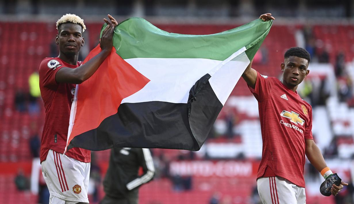 Gelandang Manchester United, Paul Pogba (kiri) dan Amad Diallo membentangkan bendera Palestina usai berakhirnya laga lanjutan Liga Inggris 2020/2021 pekan ke-37 melawan Fulham di Old Trafford Stadium, Rabu (18/5/2021). Manchester United bermain imbang 1-1 dengan Fulham. (AP/Laurence Griffiths/Pool)