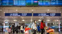Penerbangan dari Wuhan Ditutup: Pelancong berjalan melintasi papan informasi tentang penerbangan dari Wuhan telah dibatalkan di Bandara Internasional Ibu Kota Beijing pada Kamis (23/1/2020). China menangguhkan semua transportasi dari dan ke kota pusat penyebaran virus corona. (AP/Mark Schiefelbein)