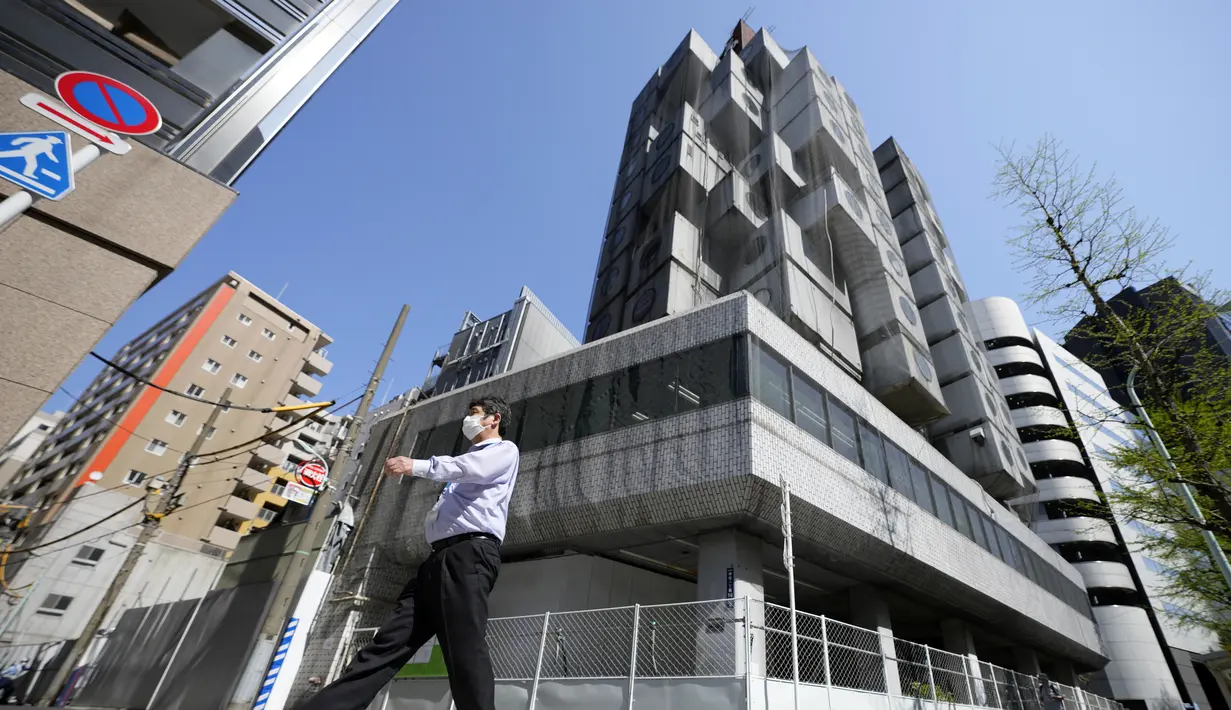 Seorang pria berjalan di depan lokasi pembongkaran Nakagin Capsule Tower, bangunan ikonik yang dirancang arsitek Jepang Kisho Kurokawa pada tahun 1972, di distrik Ginza Tokyo, Selasa (12/4/2022). Pekerjaan pembongkaran menara 140 unit kapsul tersebut dimulai Selasa. (AP Photo/Eugene Hoshiko)
