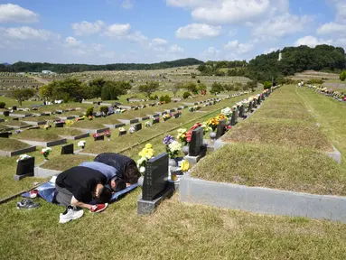 Anggota keluarga membungkuk untuk menghormati pemakaman leluhur mereka menjelang liburan Chuseok, Hari Thanksgiving versi Korea, di sebuah pemakaman di Paju, Korea Selatan (12/9/2021).  Pemakaman nasional Korea Selatan akan ditutup selama liburan Chuseok. (AP Photo/Ahn Young-joon)