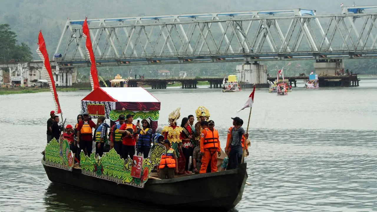 Perahu hias Festival Serayu Banyumas 2018 berlayar dengan latar Jembatan Kereta Api yang melintang di atas Sungai Serayu. (Foto: Liputan6.com/FSB 2018/Muhamad Ridlo)