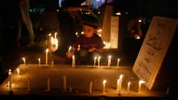 Seorang bocah memegang lilin di pemakaman keluarga dan saudara mereka saat memperingati Shab-e-Barat di pinggiran Srinagar, Kashmir (1/5). (AP Photo / Mukhtar Khan)