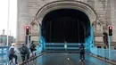 Pesepeda menunggu untuk menyeberangi Tower Bridge yang terjebak dalam posisi terbuka di pusat kota London Senin (9/8/2021). Tower Bridge London macet terbuka mengakibatkan gangguan lalu lintas di kedua sisi Sungai Thames karena mobil dan pejalan kaki tidak dapat menyeberang. (Tolga Akmen/AFP)