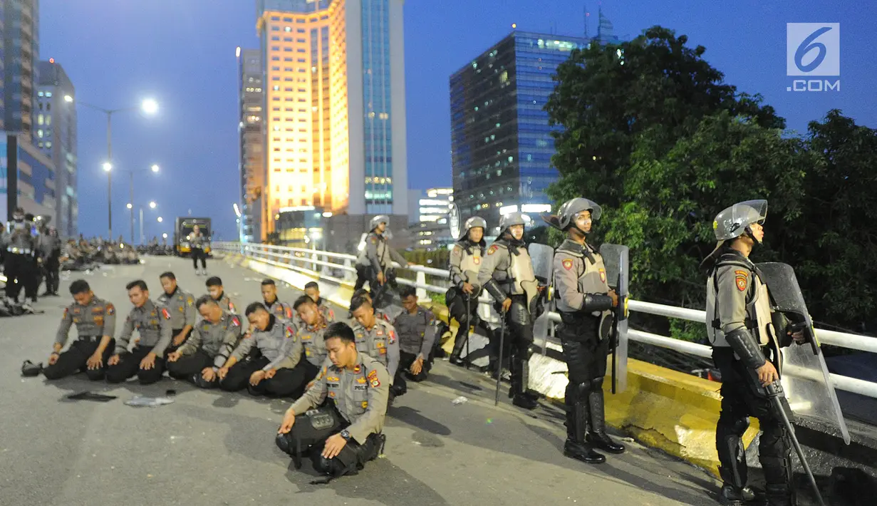 Anggota Dalmas BKO dari Polda Bali melaksanakan salat Magrib usai mengamankan perusuh di atas fly over Slipi, Jakarta, Rabu (22/5/2019). Bentrokan panjang dengan para perusuh membuat anggota kepolisian yang berhadapan langsung kurang beristirahat. (merdeka.com/Arie Basuki)