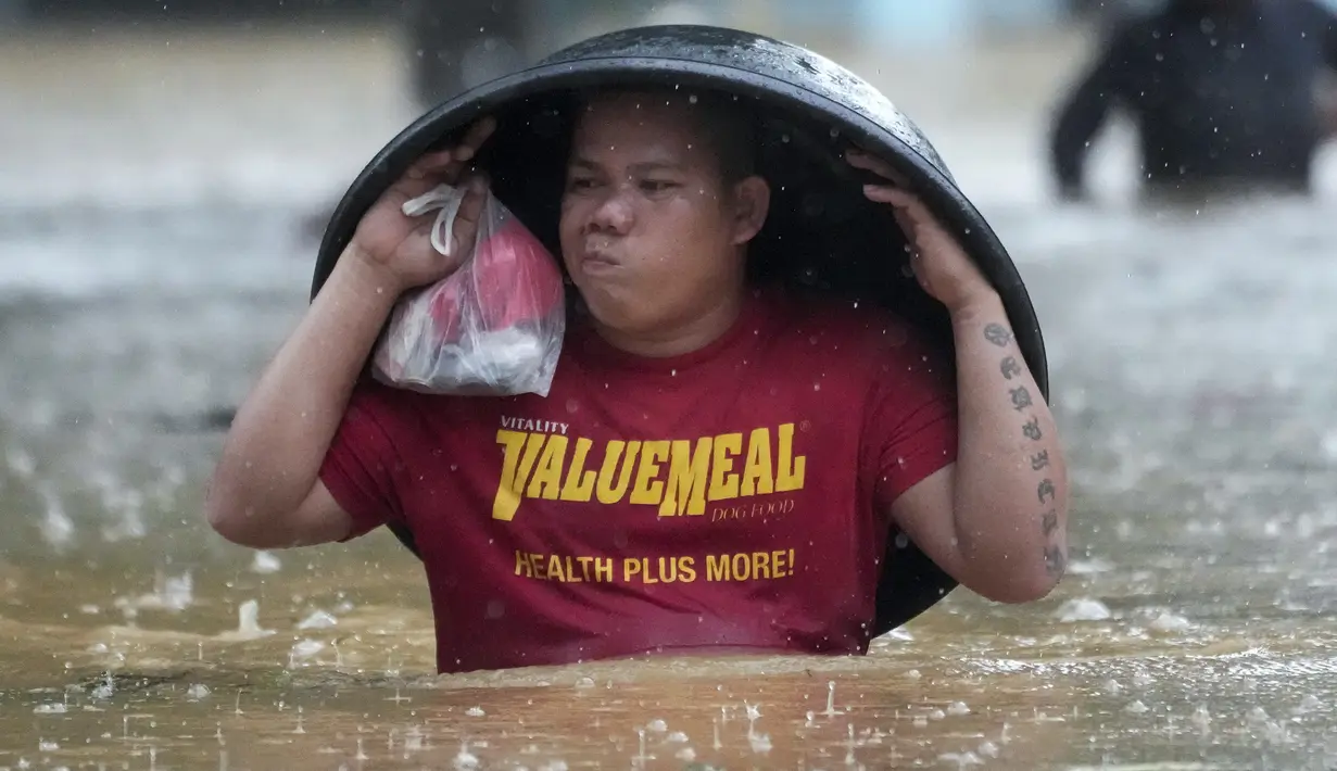 Seorang warga menggunakan bak cucian untuk melindunginya dari hujan saat ia menyeberangi jalan yang banjir akibat Badai Tropis Yagi, yang secara lokal disebut Enteng, di Cainta, provinsi Rizal, Filipina, Senin (2/9/2024). (AP Photo/Aaron Favila)