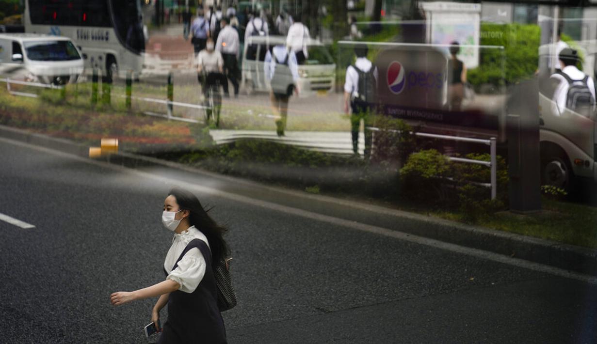 Seorang wanita berjalan di seberang jalan ketika komuter lain tercermin di jendela bus menjelang Olimpiade 2020 di Tokyo, Jepang, Rabu (14/7/2021). Keadaan darurat akan berlaku sepanjang Olimpiade yang dibuka pada 23 Juli. (AP Photo/Jae C. Hong)