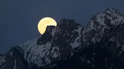 Bulan purnama tampak di belakang pegunungan Alpen yang tertutup salju di Buching, Jerman selatan, (10/5). (Karl-Josef Hildenbrand/dpa/AFP)
