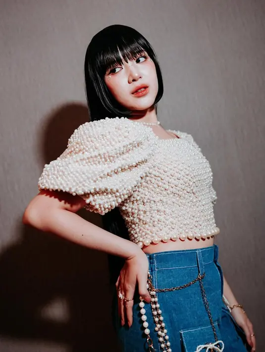 Atasan tersebut ia padukan dengan celana jeans high waist, menghadirkan perpaduan gaya klasik dan modern yang pas. Aksesori berupa kalung dan gelang mutiara senada pun menambah sentuhan manis pada keseluruhan look-nya.
